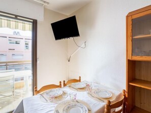 A dining area with a table set for four, a television mounted on the wall, and a wooden cabinet to the right. - Saint James by Interhome (Le Lavandou)
