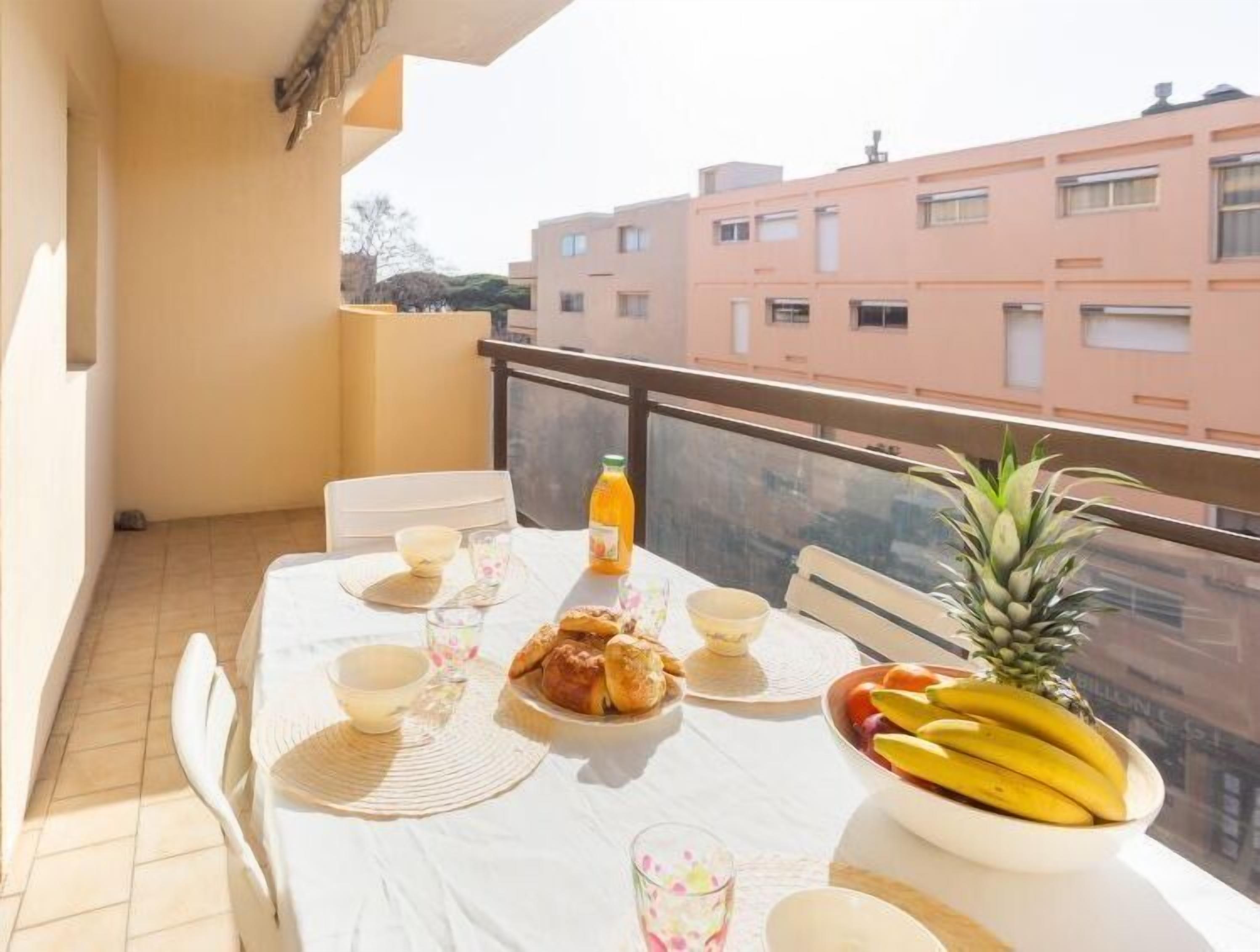 A balcony with a table set for breakfast, including bread, fruit, and a pineapple.
