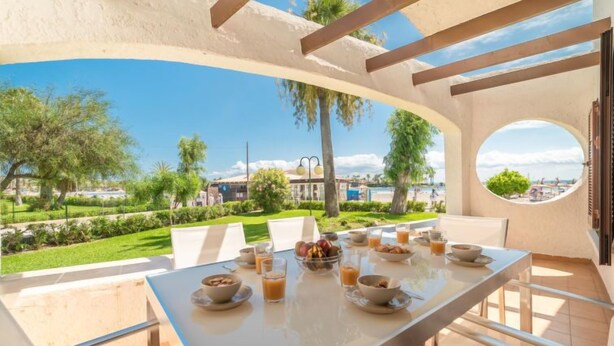 A dining area with a table set for breakfast, overlooking a landscaped garden and a view of the sea. - Carabela Front Beach & Pool by Interhome (Port d'Alcúdia)