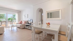 A spacious living area with a glass dining table, white furniture, and a TV. - Carabela Front Beach & Pool by Interhome (Port d'Alcúdia)