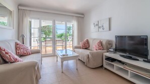 A modern living room with a sofa, a coffee table, and a TV. There is a sliding glass door leading to an outdoor area. - Carabela Front Beach & Pool by Interhome (Port d'Alcúdia)