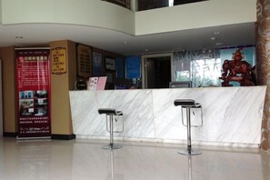 Zona de recepción de un hotel con un mostrador de mármol, dos taburetes de bar y una estatua.