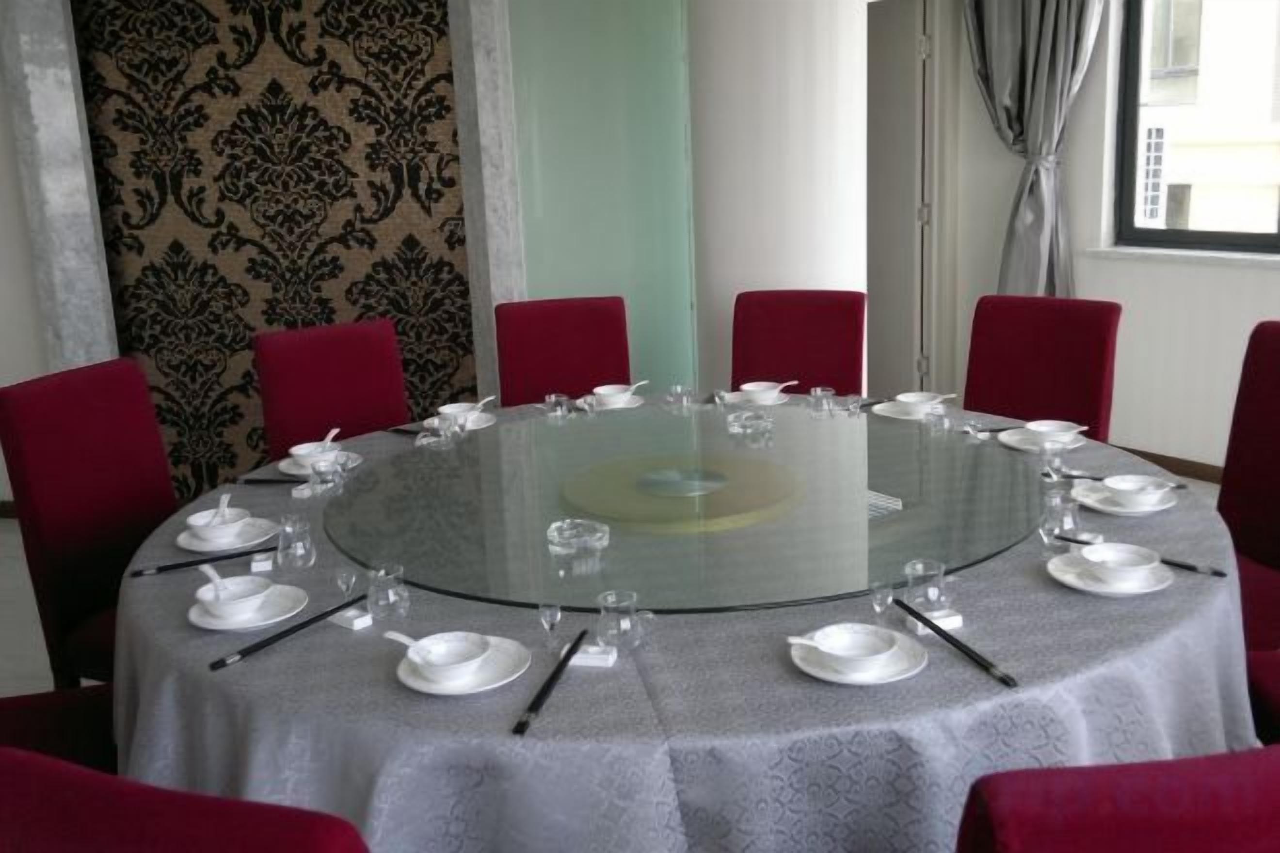 A round glass table with white plates and cutlery, surrounded by red chairs.
