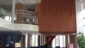 Vestíbulo de hotel de varios niveles con una escalera central, zonas de estar y un gran panel vertical.