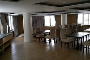 Un comedor amplio con varias mesas y sillas, ventanas grandes y un techo alto con vigas a la vista.