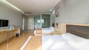Habitación de hotel con cama, escritorio, televisor y baño visible a través de una puerta de vidrio.