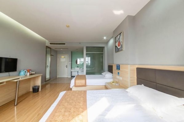 A hotel room with a bed, a desk, a TV, and a bathroom visible through a glass door.