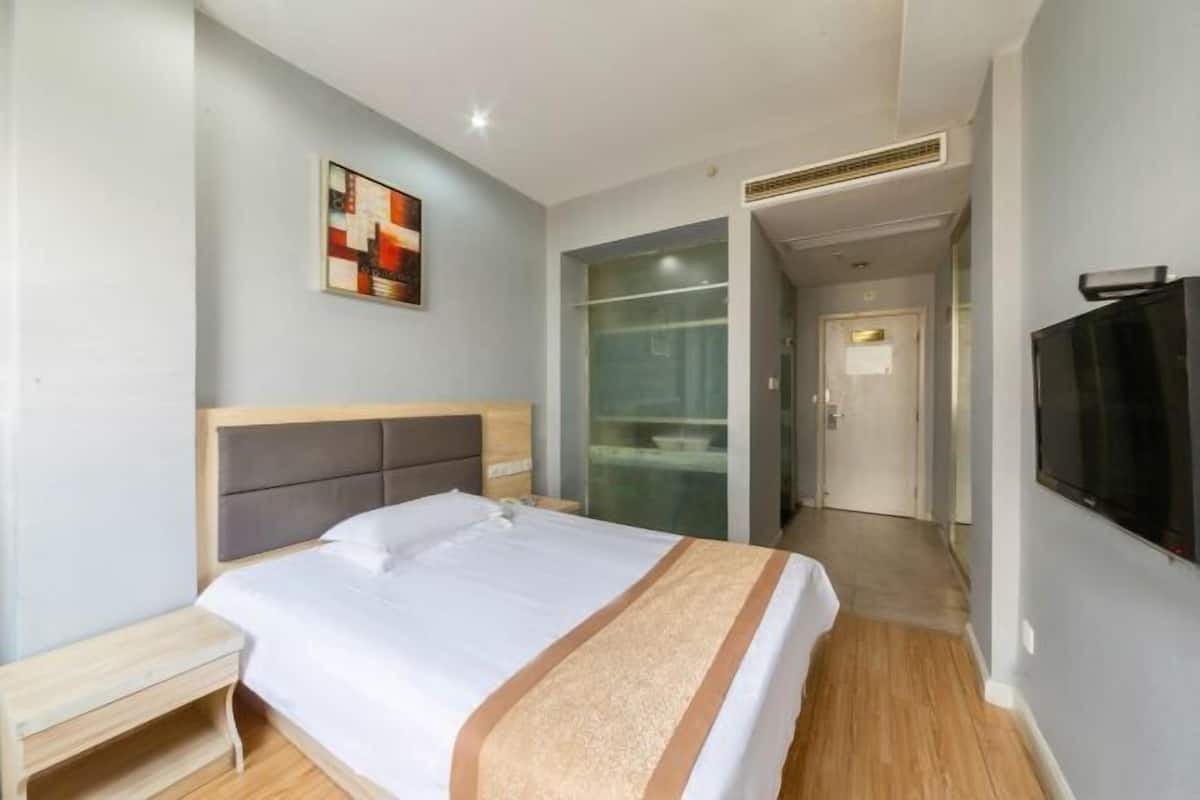 Ein Hotelzimmer mit Bett, Nachttisch, Fernseher und einer Glastür zum Badezimmer.