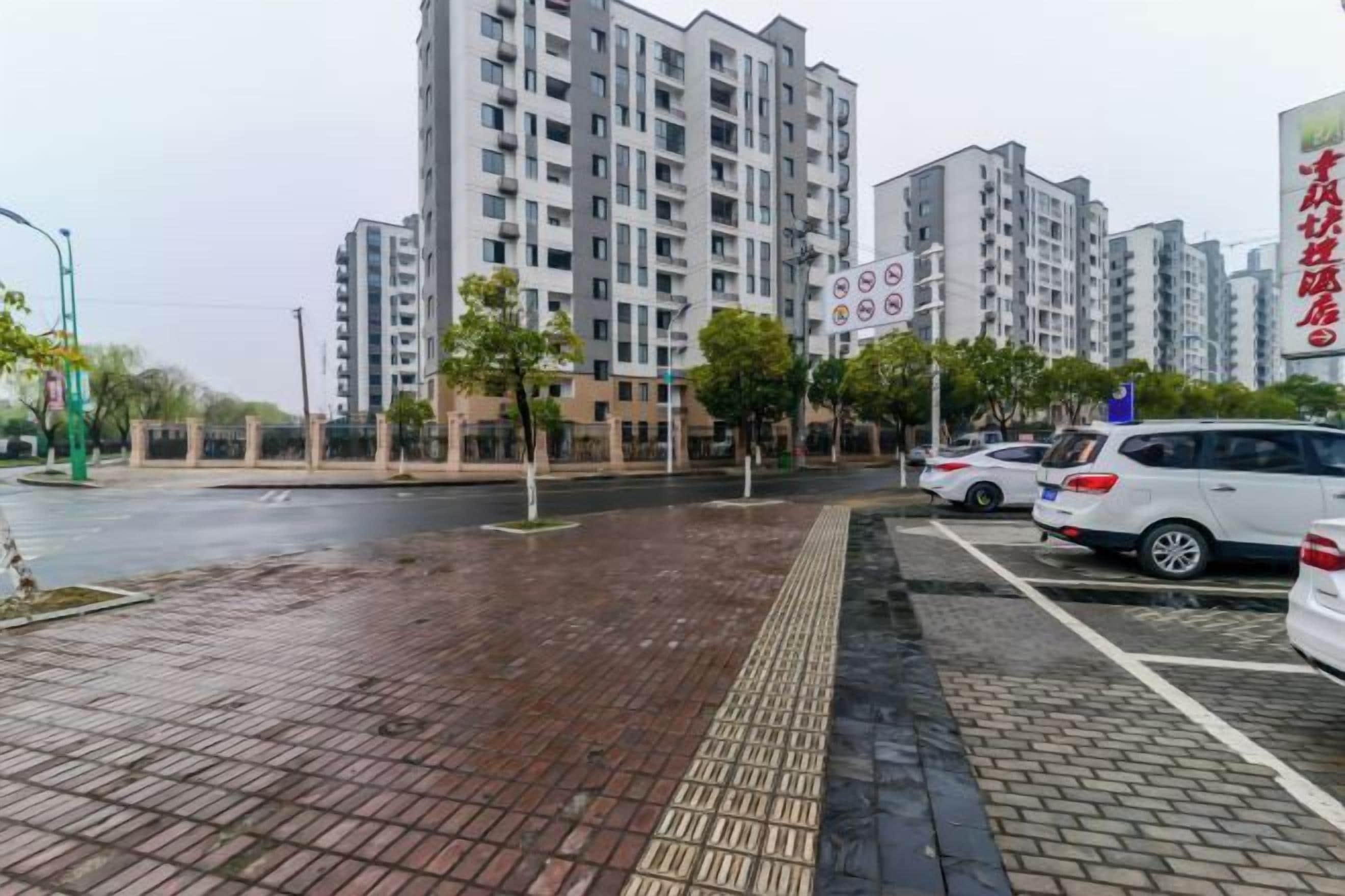 A parking area with cars, a brick pathway, and a building with multiple floors in the background.