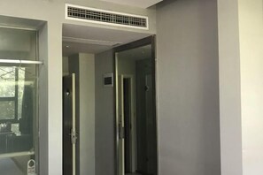 Una habitación de hotel moderna con un ventanal grande, una puerta que da a otra habitación y un sistema de ventilación en el techo.