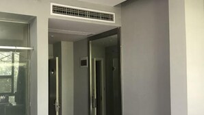 Una habitación de hotel moderna con un ventanal grande, una puerta que da a un pasillo y una rejilla de ventilación en el techo.