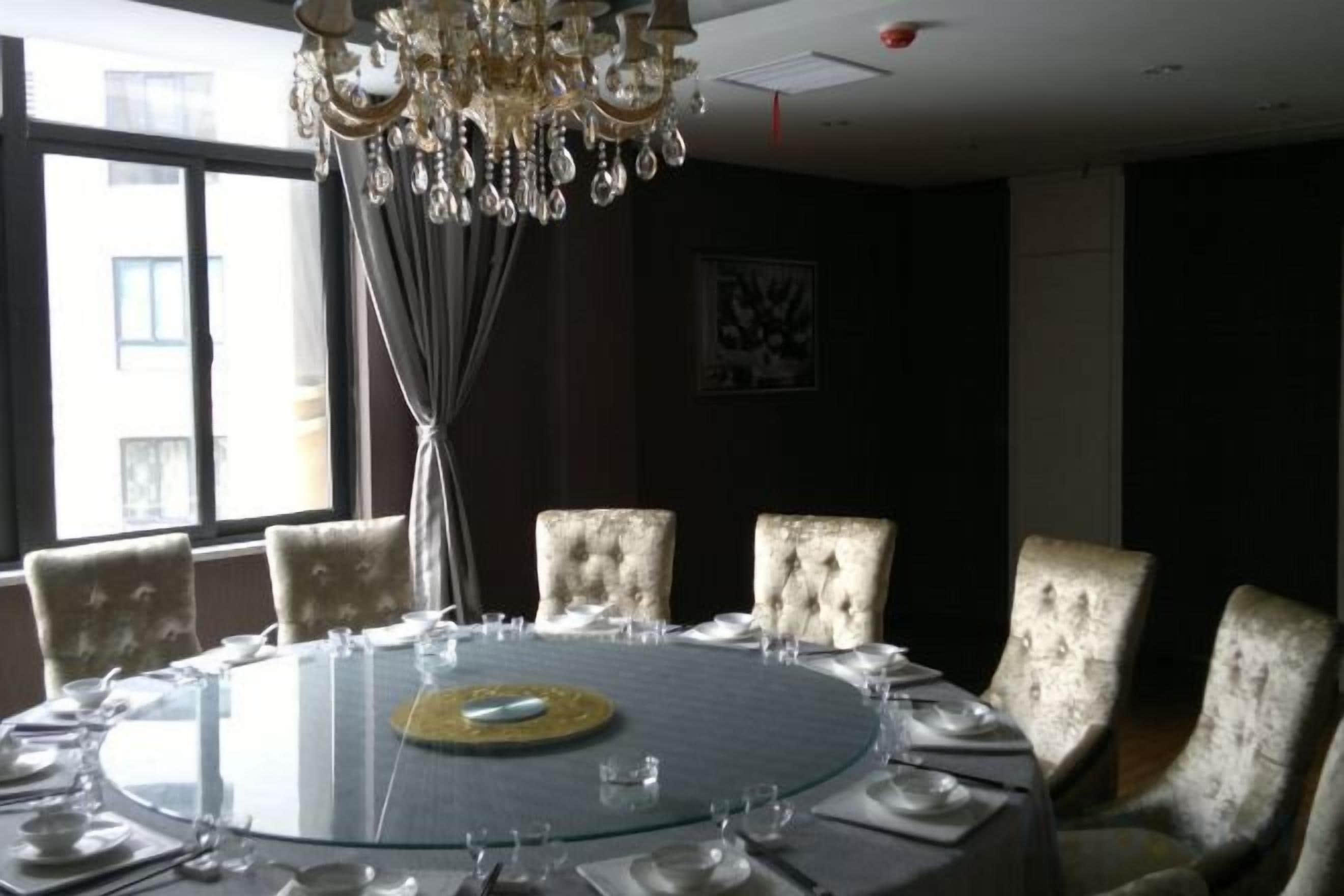 A round table with chairs, a chandelier, and a window with curtains.