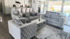 A modern living room with a grey sofa set, a coffee table, and a kitchen area with white cabinets and a microwave. - Endless Summer Villa with heated salt water pool (Port Charlotte)