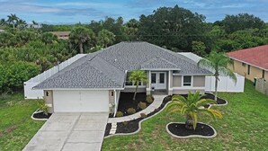 A single-story house with a grey tiled roof, a front porch, and a small front yard with a palm tree. - Endless Summer Villa with heated salt water pool (Port Charlotte)