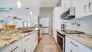 A modern kitchen with white cabinetry, granite countertops, stainless steel appliances, and pendant lighting. - Endless Summer Villa with heated salt water pool (Port Charlotte)