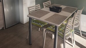 A compact kitchen with a refrigerator, microwave, and a clock on the wall. There is a dining table with chairs and a flat-screen TV mounted on the wall. - Zenitude AZ75 (Frejus)