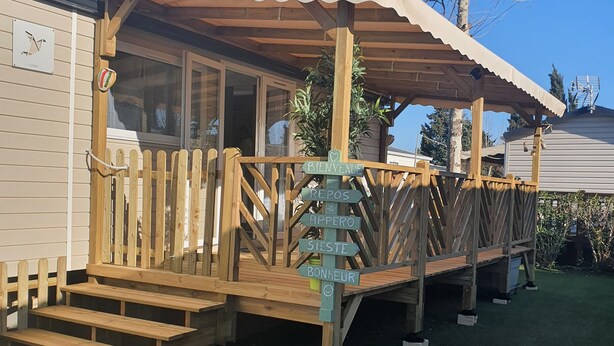 A wooden deck with a covered area, steps leading up to a building, and a signpost with directional signs. - Zenitude AZ75 (Frejus)
