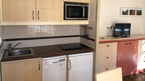 A compact kitchen with wooden cabinets, a microwave, a dishwasher, and a small countertop with a television. - Cap Esterel Agay - large garden - exceptional sea and pool views (Saint-Raphaël)