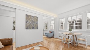 A spacious living area with a wooden floor, a round coffee table, a sofa, and a dining table with chairs. - Mulwarree Avenue Apartments by Urban Rest (Randwick)