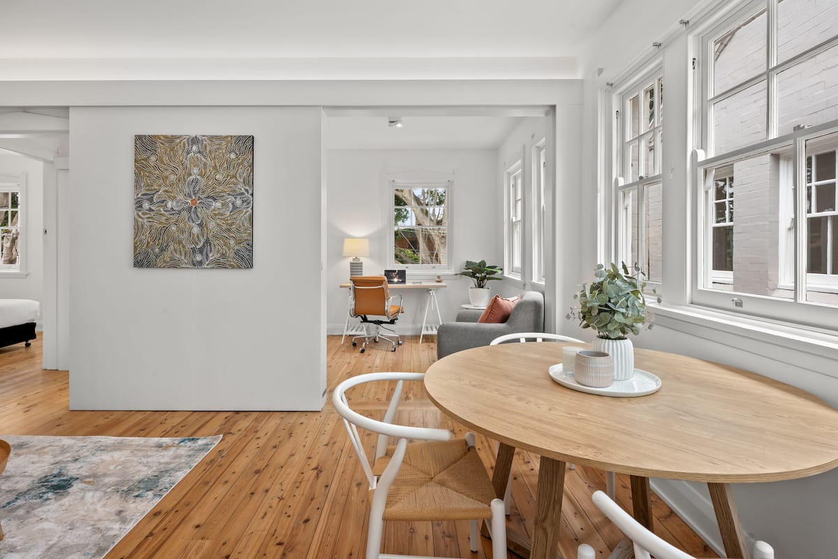 Ein modernes Wohnzimmer mit einem Holzesstisch, weißen Stühlen und einem großen, abstrakten Gemälde an der Wand.
