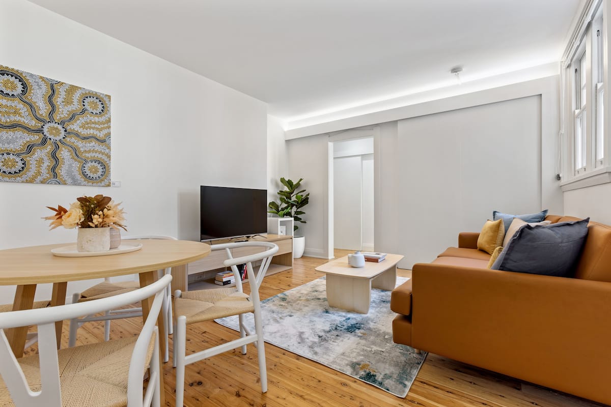 Ein modernes Wohnzimmer mit einem runden Esstisch, weißen Stühlen, einer Couch, einem Couchtisch und einem Flachbildfernseher.