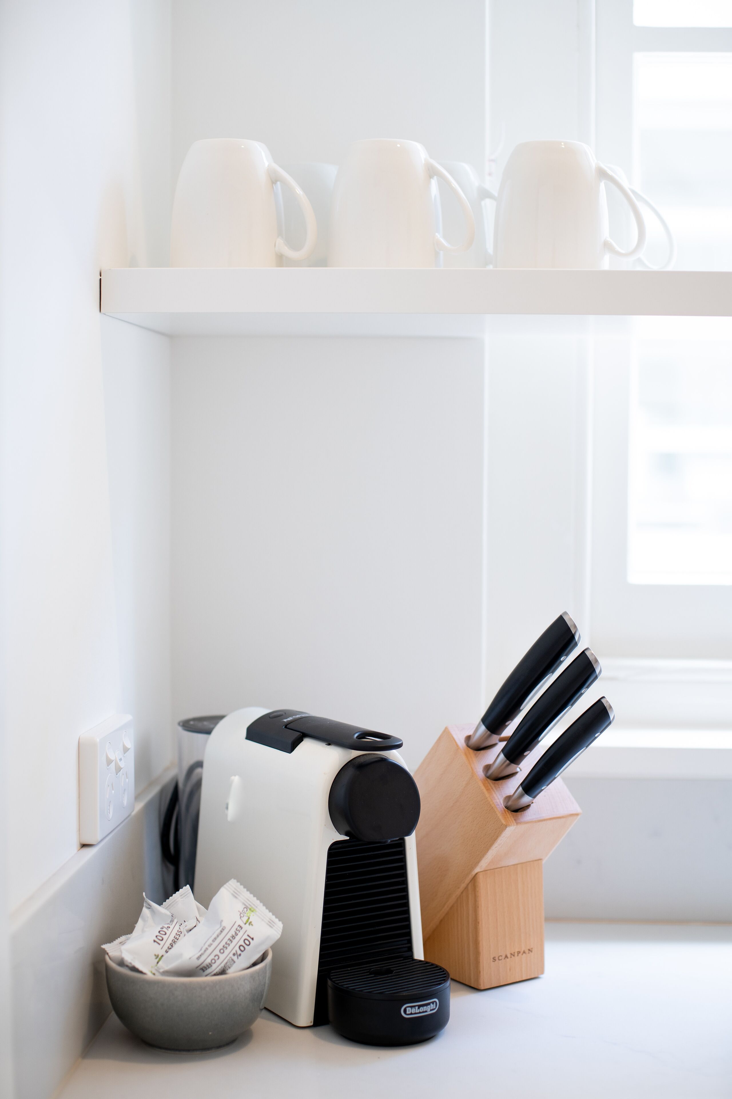 A kitchen counter with a coffee maker, a knife block, and a bowl of coffee packets.