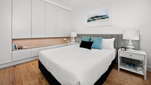 A modern bedroom with a large bed, white nightstands, a headboard, and a wall-mounted artwork. - Mulwarree Avenue Apartments by Urban Rest (Randwick)