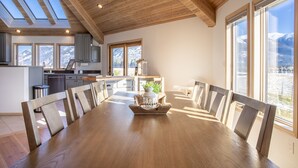Un comedor amplio con una mesa y sillas de madera, ventanas grandes con vistas a la montaña y una cocina con electrodomésticos modernos.