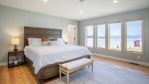 Un dormitorio con una cama grande, mesitas de noche, un banco y vistas al exterior a través de amplios ventanales.