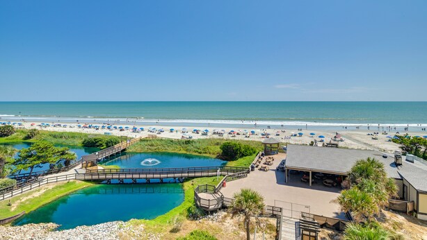 Un resort sulla spiaggia con piscina, passerella e ombrelloni.