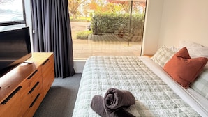 A bedroom with a bed, a TV, a wooden dresser, and a sliding glass door leading to an outdoor area. - Location Location! T Two on Whakaue  (Rotorua)