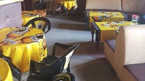 A restaurant with yellow tablecloths, black chairs, and a television screen in the background. - Kapsabet Comfy Hotel (Kapsabet)