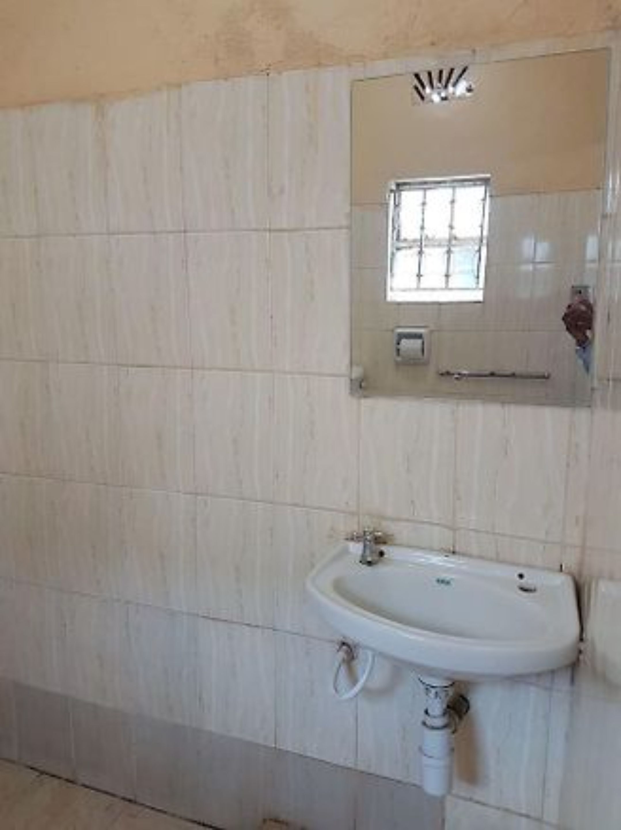 Une salle de bain avec un lavabo blanc, un miroir au-dessus et une fenêtre avec des barreaux.