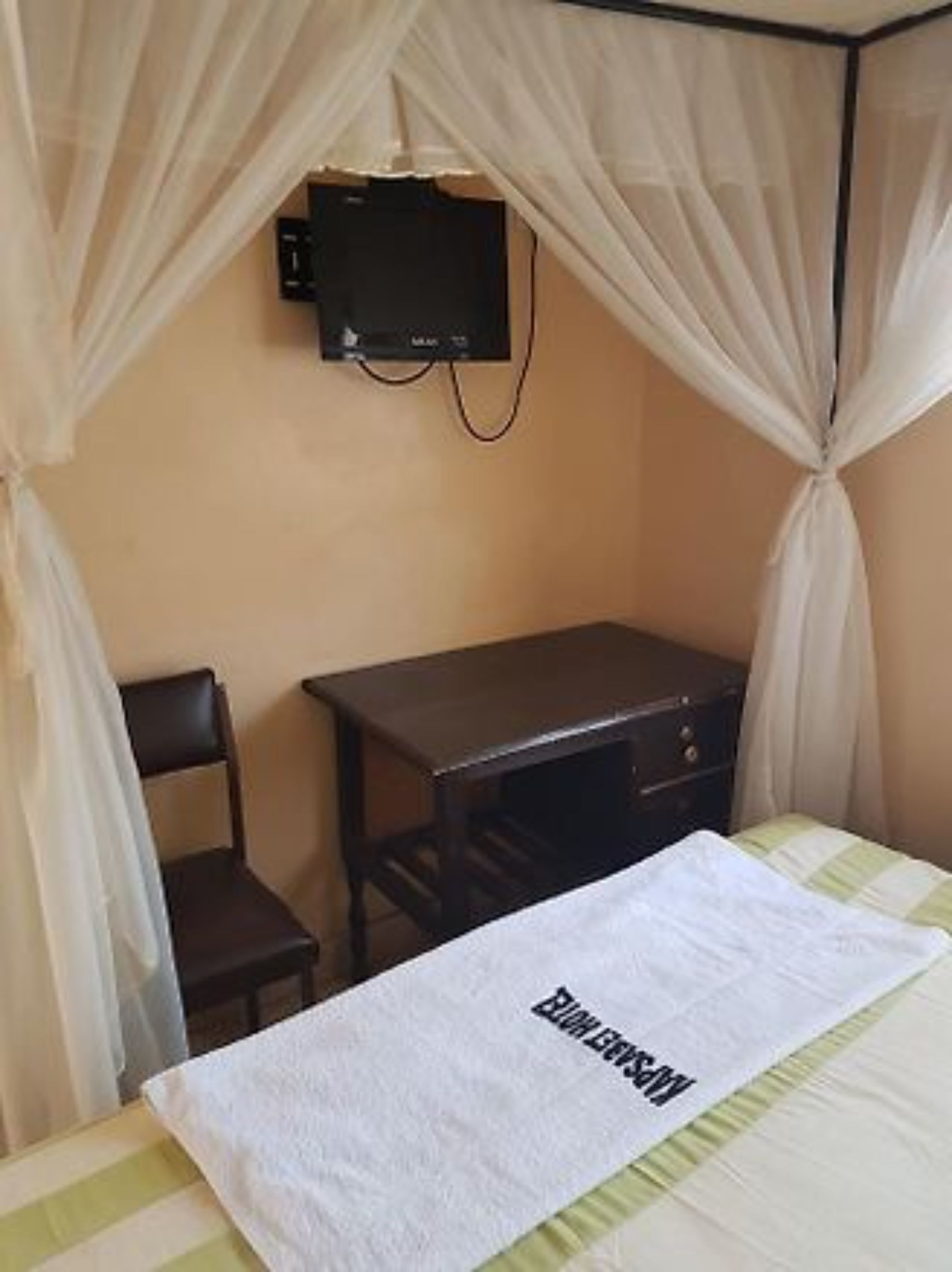 A bedroom with a bed, a desk, a chair, and a television mounted on the wall.