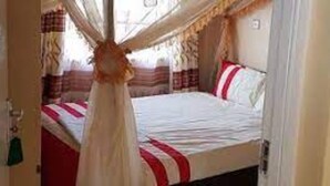 A bedroom with a canopy bed, a bedside table, and a window with curtains. - Kapsabet Comfy Hotel (Kapsabet)