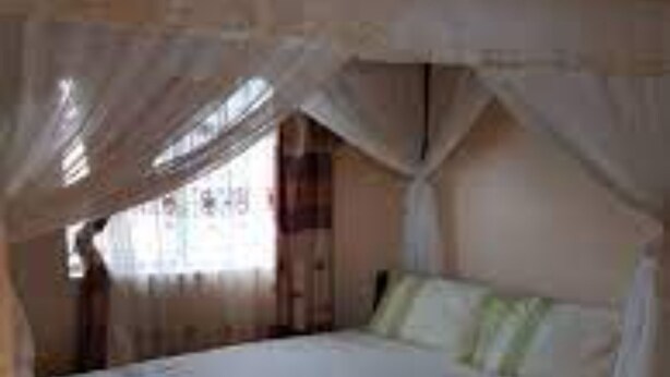 A single bed with a canopy, a bedside table, and a window with curtains. - Kapsabet Comfy Hotel (Kapsabet)
