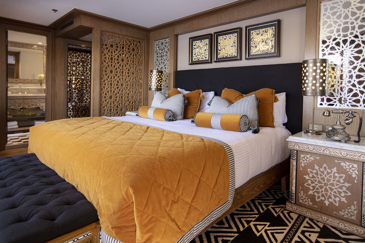Une chambre élégamment aménagée, dotée d’un grand lit, d’une table de chevet et d’œuvres d’art décoratives au mur.