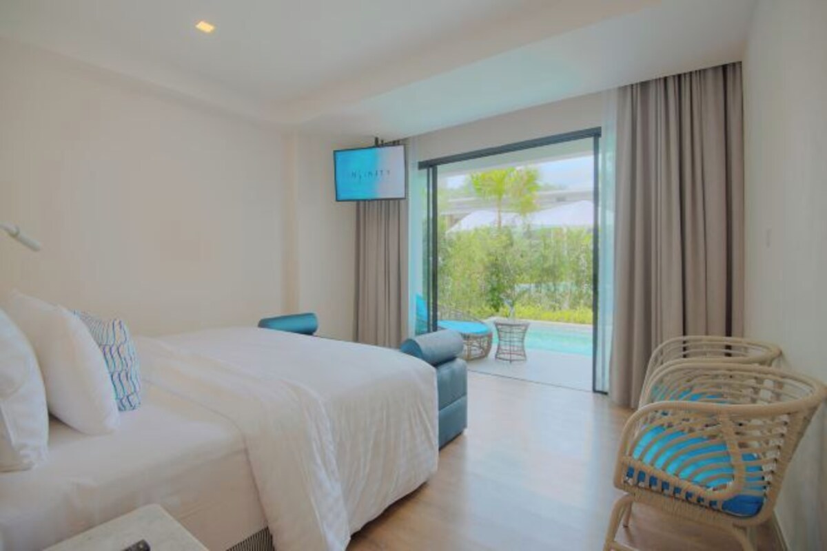 A hotel room with a bed, a TV, a balcony with a view, and wicker chairs.