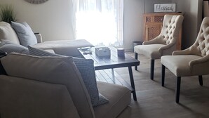 A living room with a sofa, two armchairs, a coffee table, a TV, and a ceiling fan.