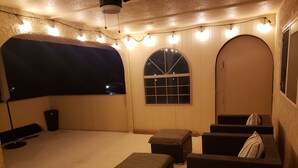 A cozy outdoor seating area with a covered section, cushioned seating, and string lights.