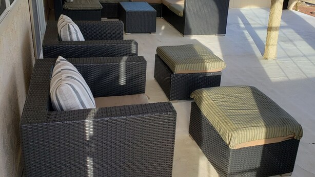A covered outdoor seating area with wicker furniture and a ceiling fan.