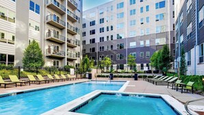 A swimming pool with lounge chairs and a pool deck, surrounded by multi-story buildings with balconies. - 4th Street Suites - Deluxe King Bed Suite (Louisville)