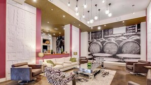 A modern living room with a sofa, coffee table, and chairs, a patterned rug, and a large wall mural. - 4th Street Suites - Deluxe King Bed Suite (Louisville)