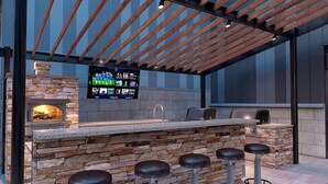 An outdoor bar area with a stone counter, bar stools, a television screen, and a wood-paneled ceiling. - 4th Street Suites - Deluxe King Bed Suite (Louisville)