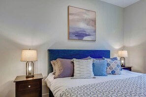 Une chambre à coucher bien rangée, avec un grand lit, deux tables de chevet et un tableau accroché au mur.