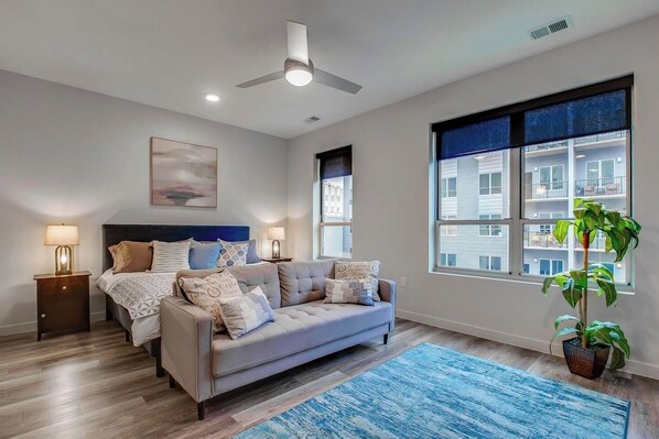 Une chambre moderne avec un lit, un canapé, un ventilateur de plafond, une grande fenêtre et une plante en pot.