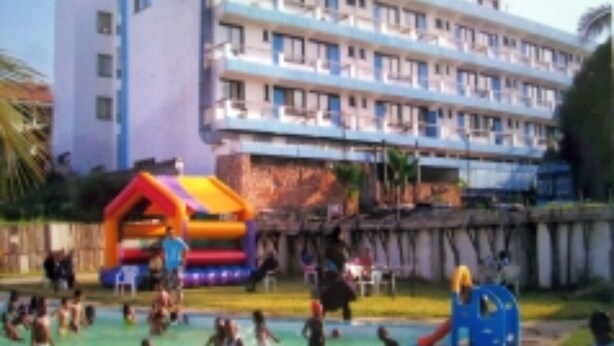 Un hotel con varios pisos, piscina y área de juegos infantiles con estructuras inflables.