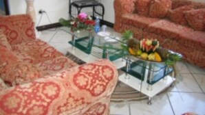 Una sala de estar con sofás estampados, un televisor sobre un mueble bajo y un frutero en una mesa de centro.