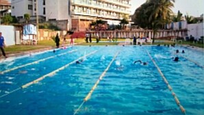 Una piscina con carriles, rodeada de edificios y un área verde.