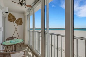Un balcon avec une table en verre et des chaises en osier, donnant sur une plage.